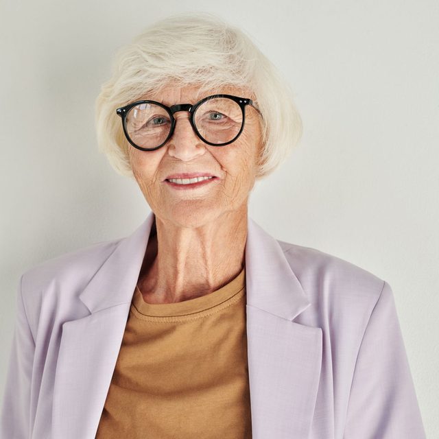 Femme senior à lunettes rondes, blazer clair, sourire discret