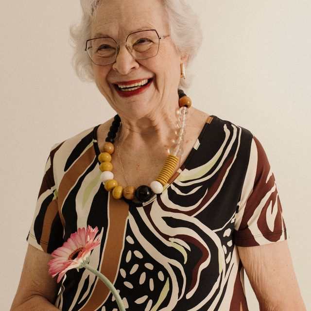 Femme âgée en blouse à motifs, collier ambré, sourire