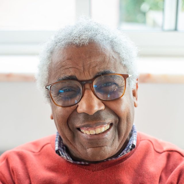 Homme senior à lunettes en pull orange, sourire ouvert