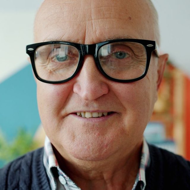 Homme senior aux grandes lunettes noires, intérieur chaleureux